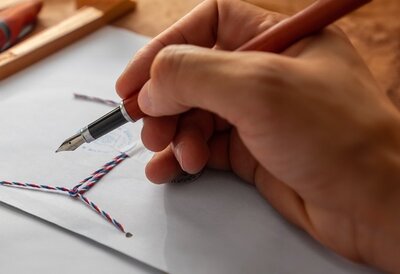 Hand schreibt mit einem Füller auf ein Dokument neben einem versiegelten Umschlag.